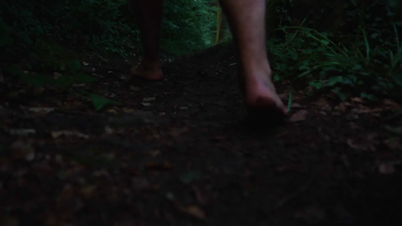 Closeup of mans feet walking barefoot in slow motion down a path in an dark forrest