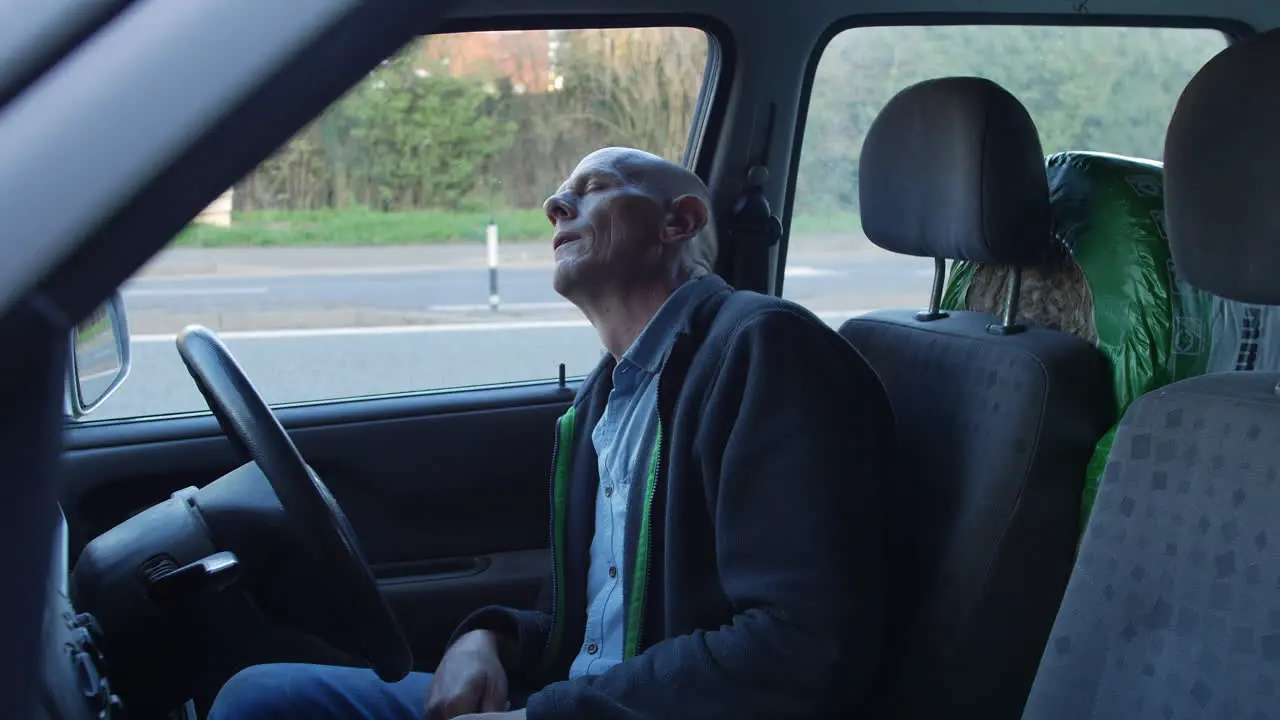 A mature man sleeping in his car at the side of a busy road