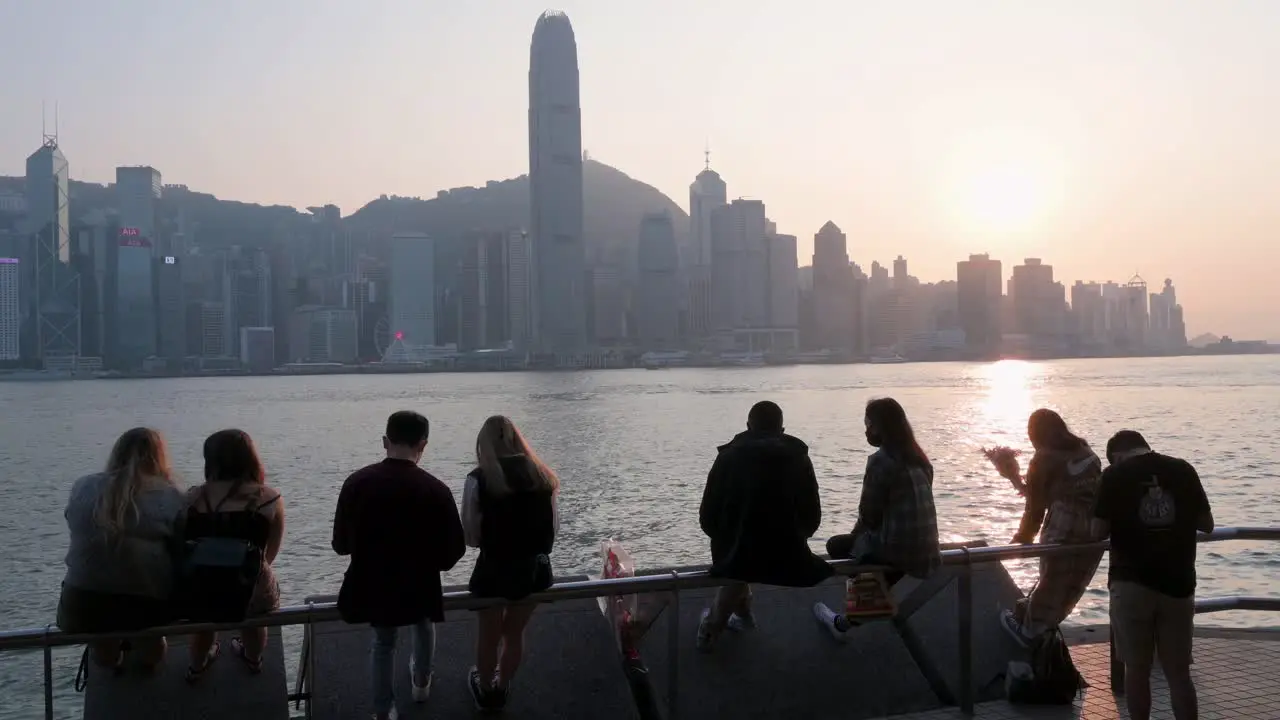 People gather along the Victoria Harbour waterfront as they enjoy the view of the Hong Kong skyline while the sunset sets in