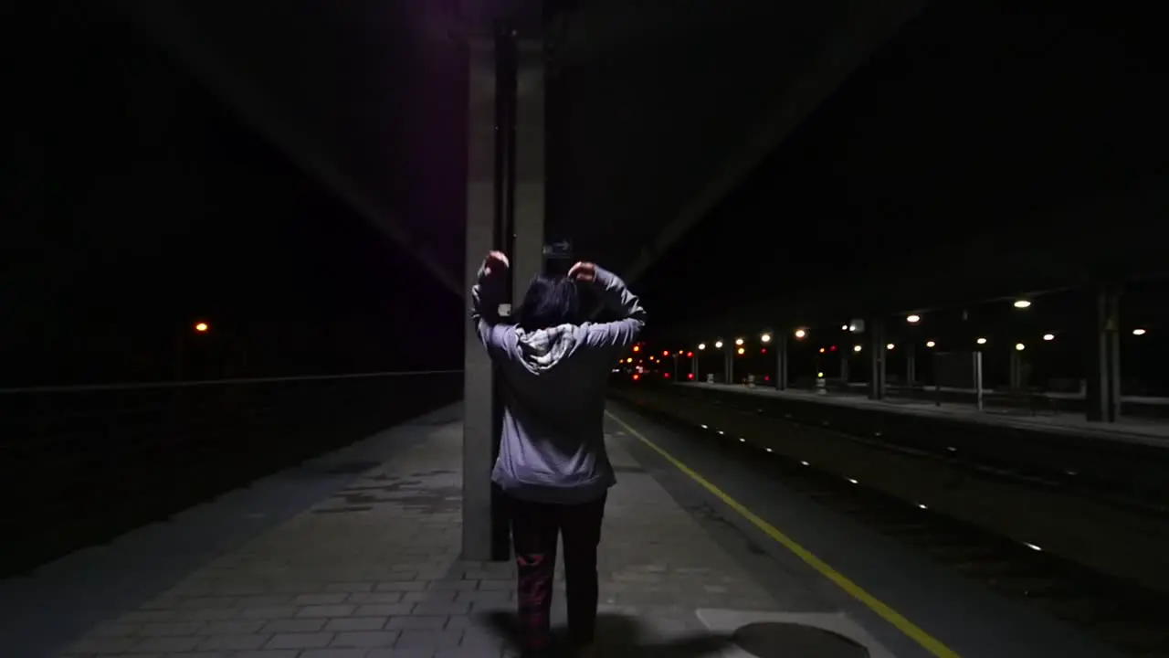 Total shot of a girl putting a hoody on a train station at night