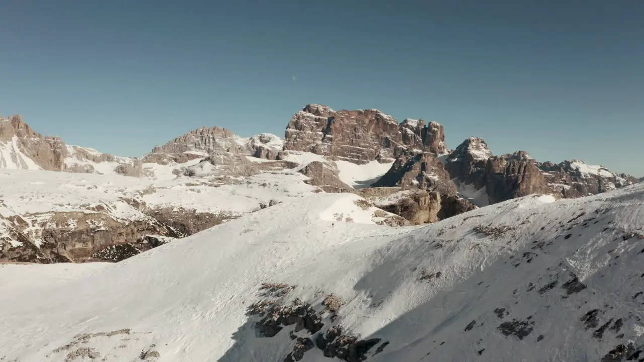 Dolly back drone shot of hiker walking along a steep snowy ridge