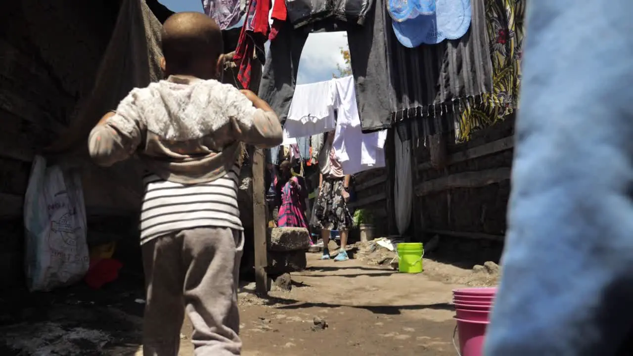 Young African kids childen walking through a poor village slums while passing laundry following tracking shot 180fps slowmotion