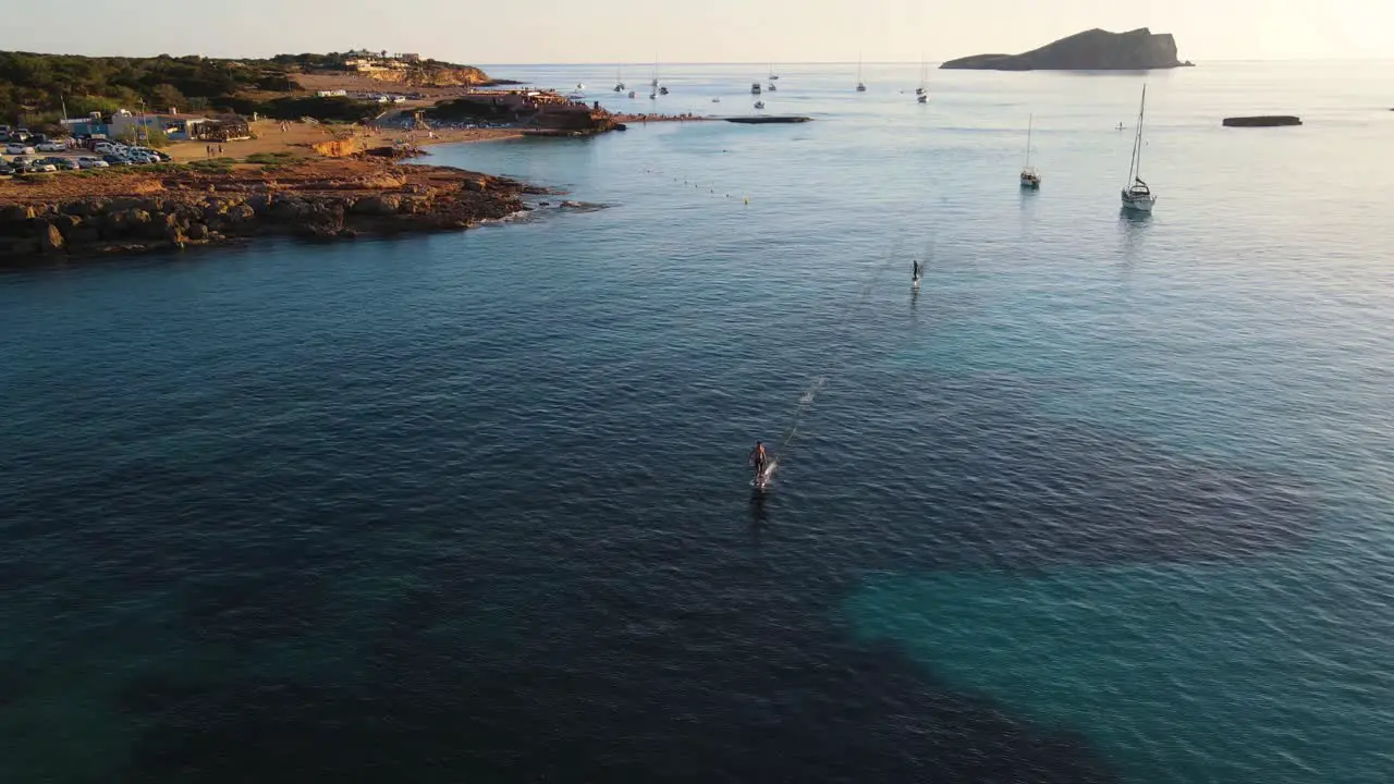 Aerial wide landscape shot of people surfing with an eFoil electric surfboard at Cala Escondida in Ibiza Spain