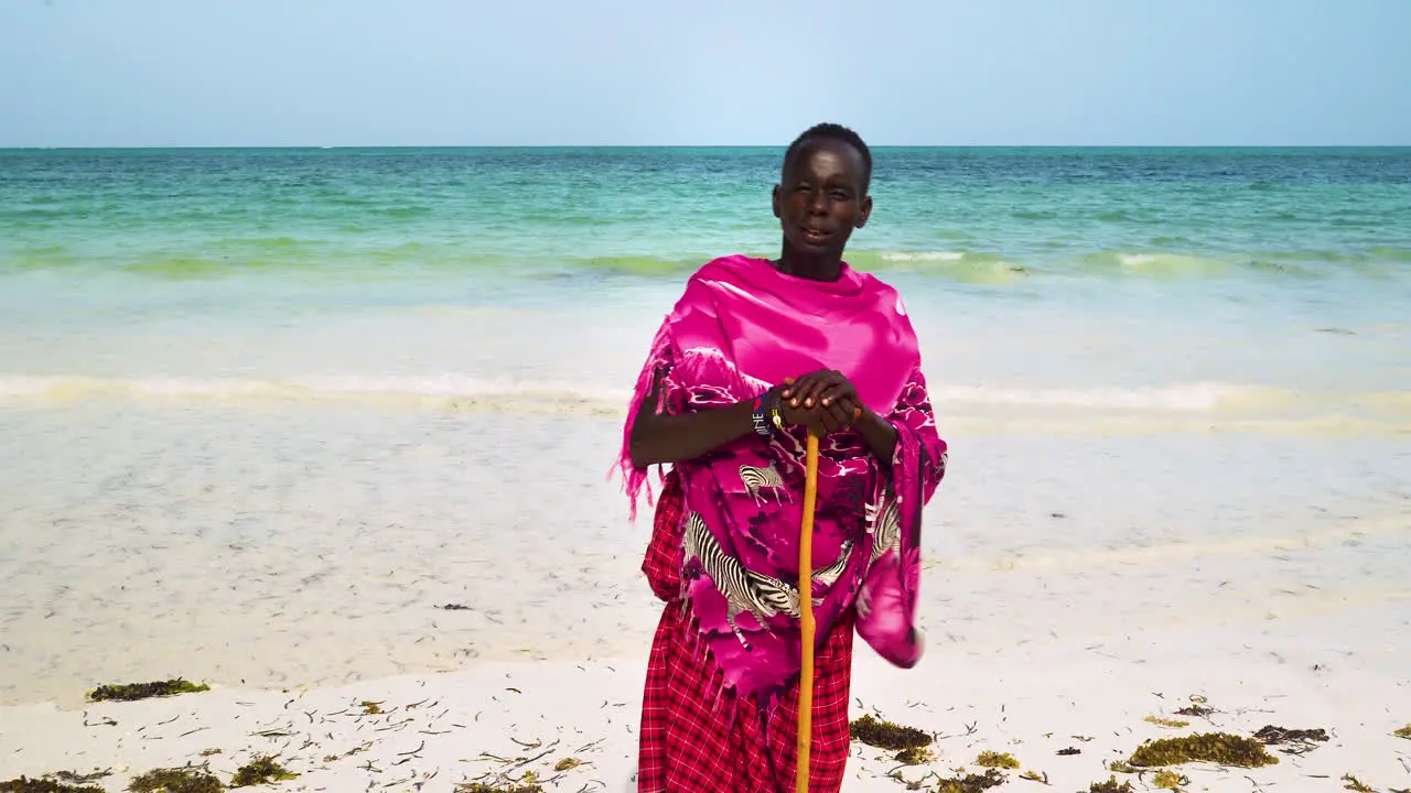 Native african man in pink clothing holding stick stands on sand beach