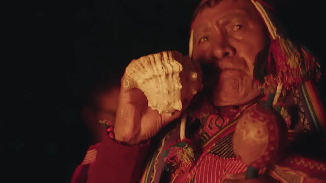 Closeup of a Quero Shaman blowing into a horn in front of a fire during night