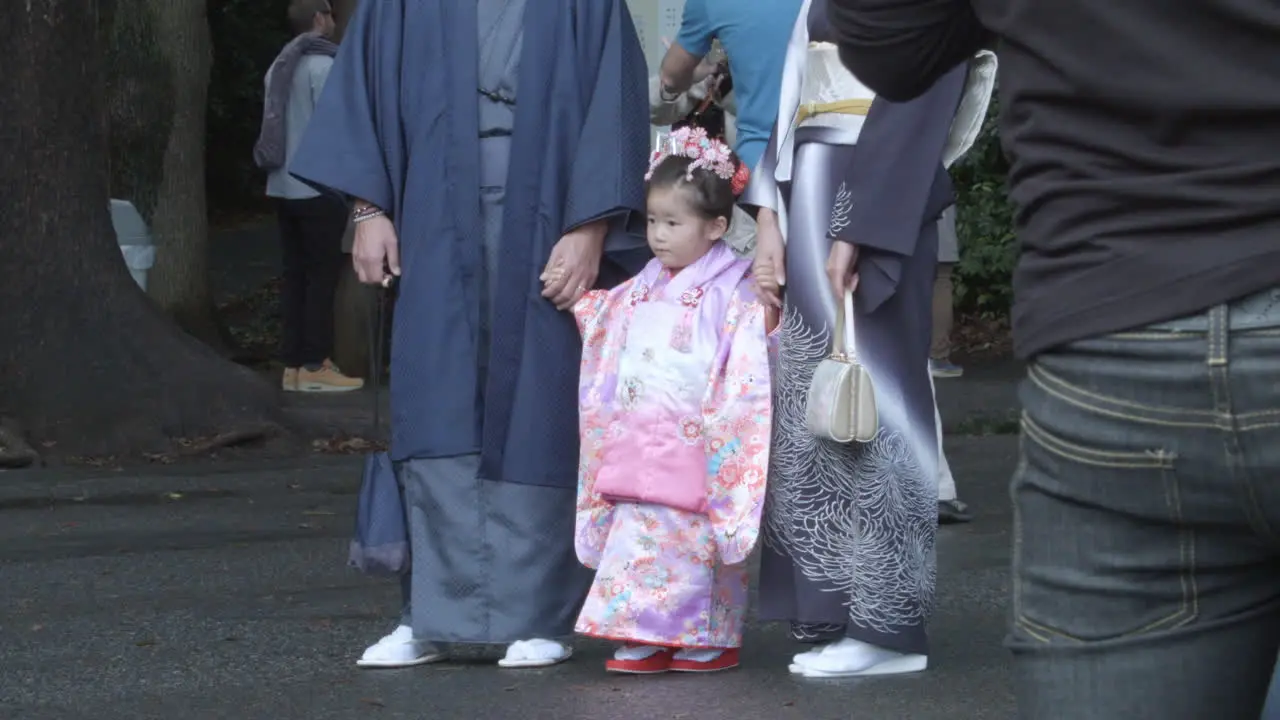 Little Japanese child in traditional Kimono attire standing still with two adults with crowds looking on