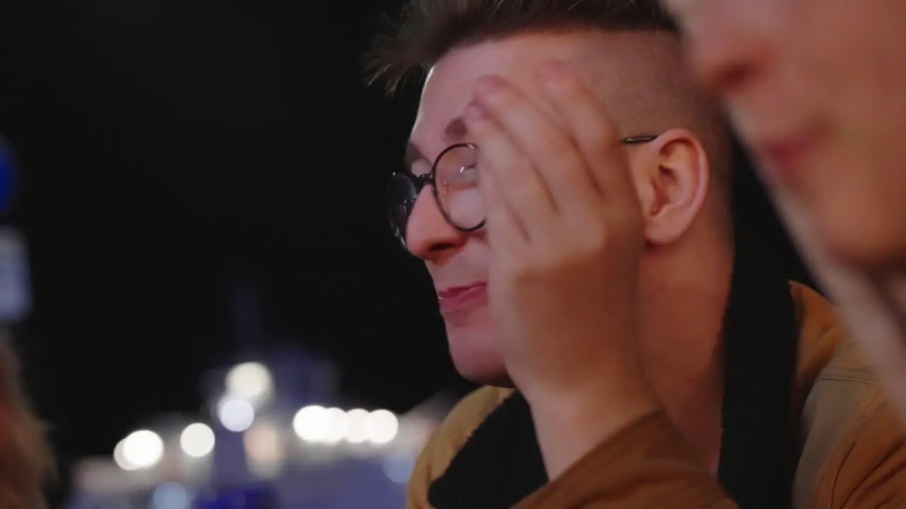 Young man wearing glasses chatting at night in outdoor social setting