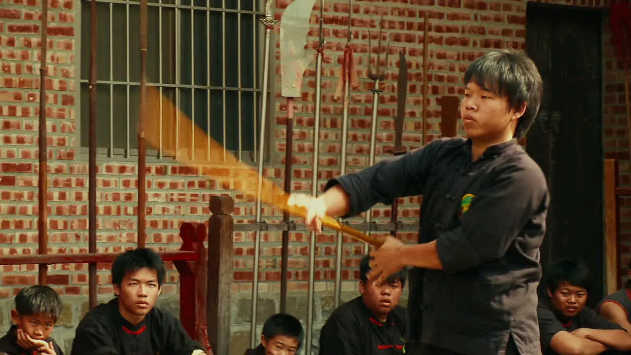 Young man twirls kung fu spear as other martial arts students watch