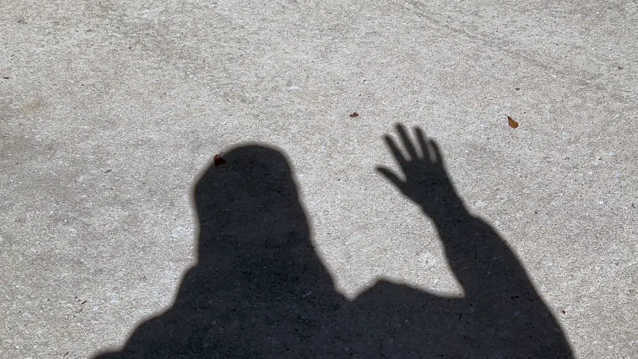 Shadow of man waving hand that is open showing all fingers standing on concrete