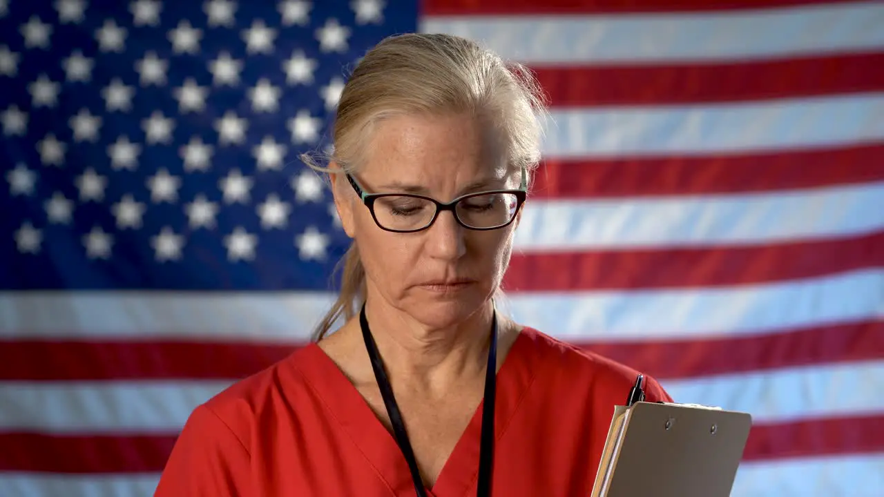 Portrait of nurse set against an out of focus US flag showing disappointment and sadness