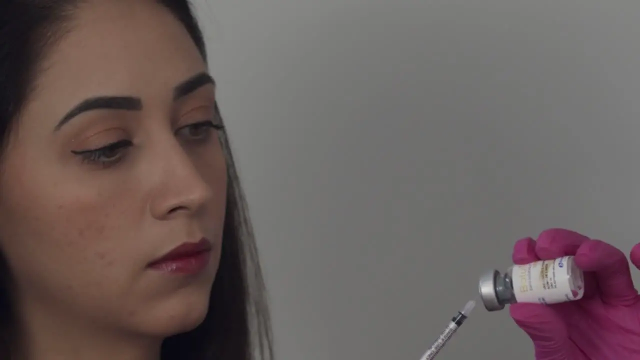 Iranian woman nurse sticking syringe needle into medical vial in slow motion