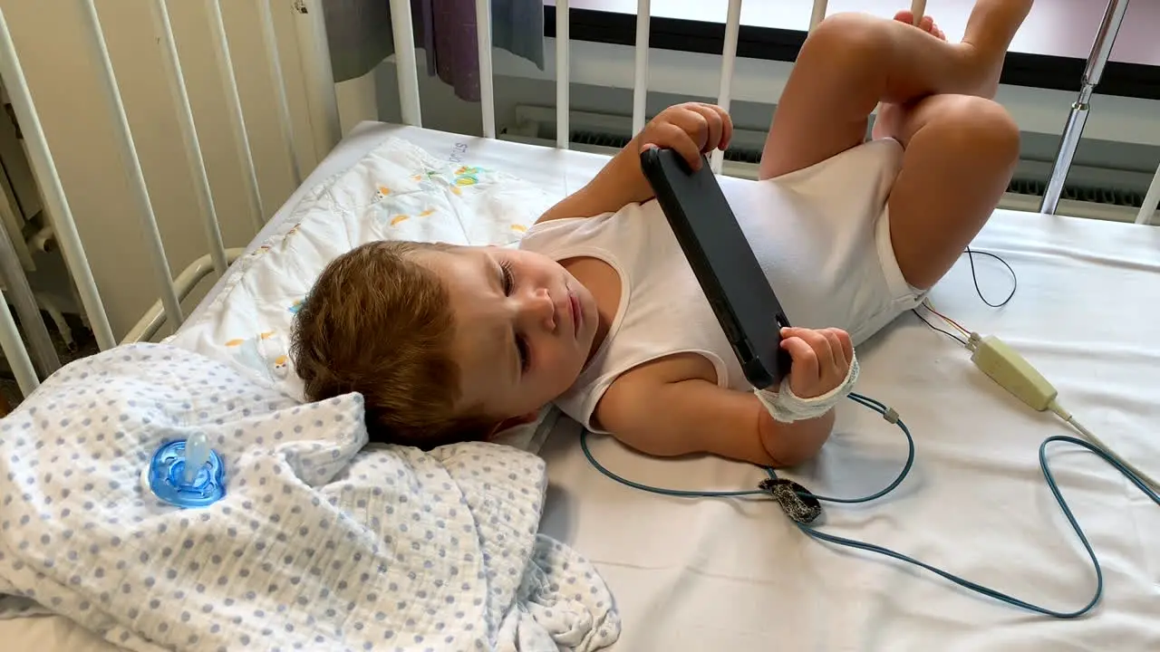 Baby boy in hospital bed watching movies on smartphone