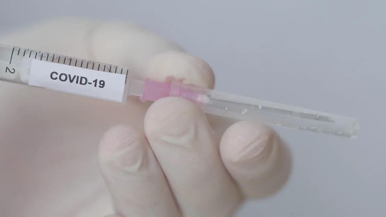 Attaching Hypodermic Needle With Plastic Cap To Syringe With Fluid And Covid-19 Label close up