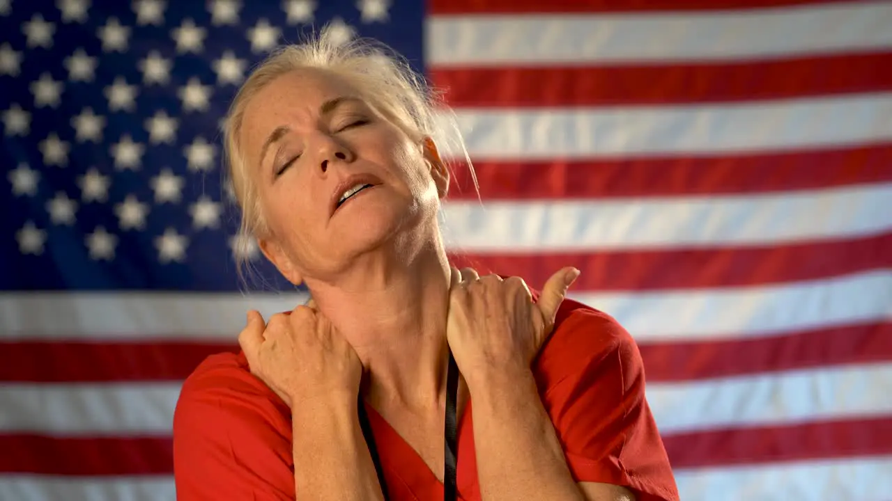 Medium tight portrait of nurse looking overwhelmed and stressed hands on her neck with American flag behind her