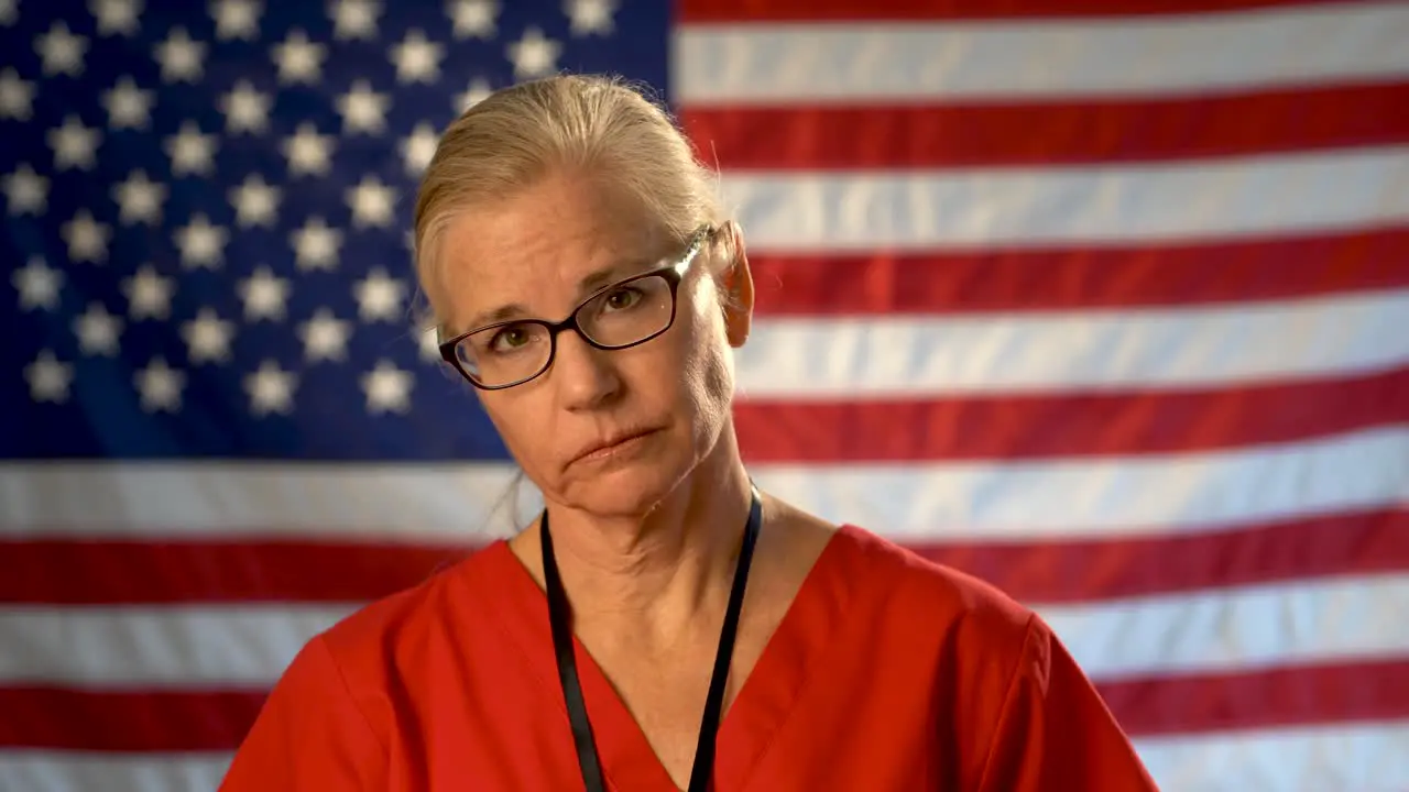 Medium tight portrait of nurse looking concerned and sad putting her glasses on with American flag behind her