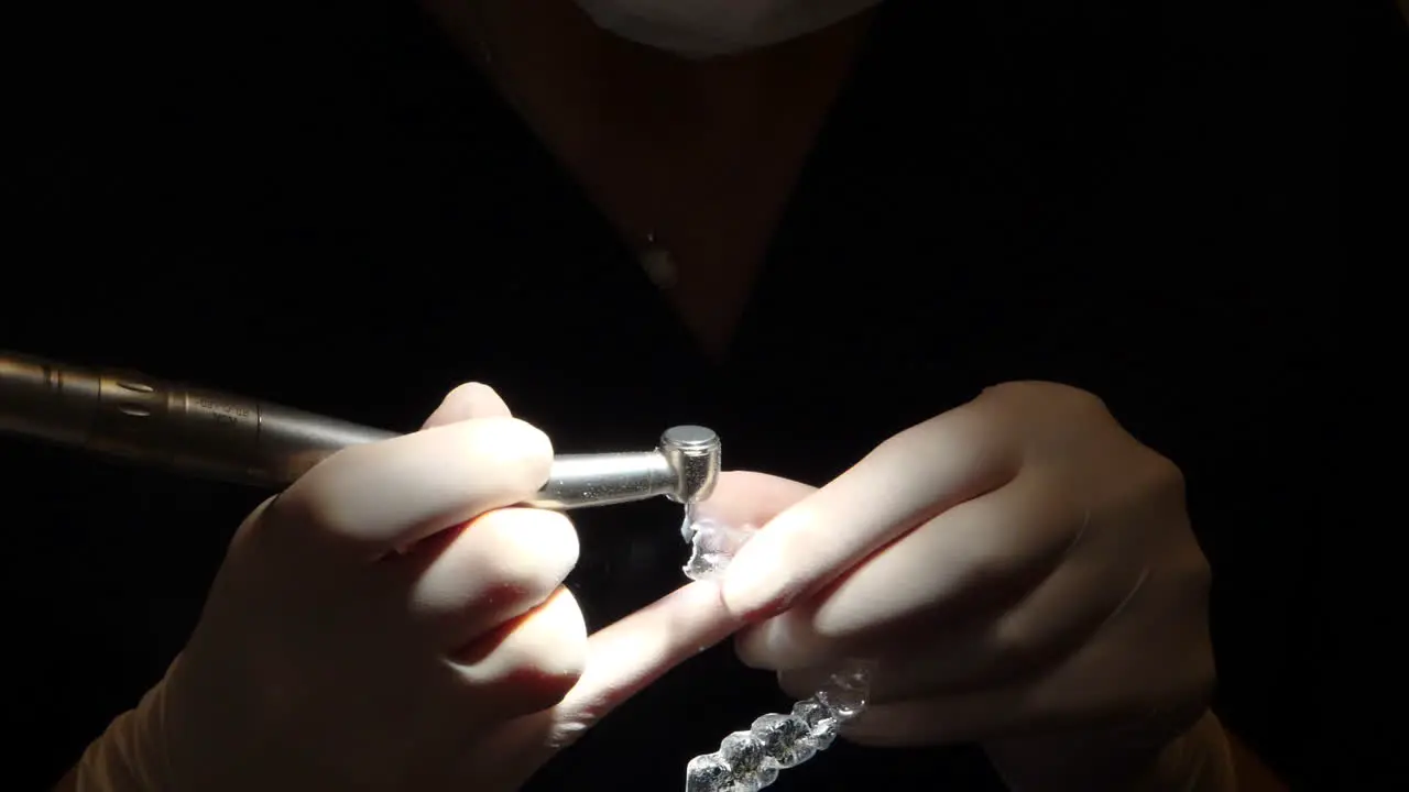 close-up view of orthodontist hands working on an invisalign aligner in dark setting with focus light