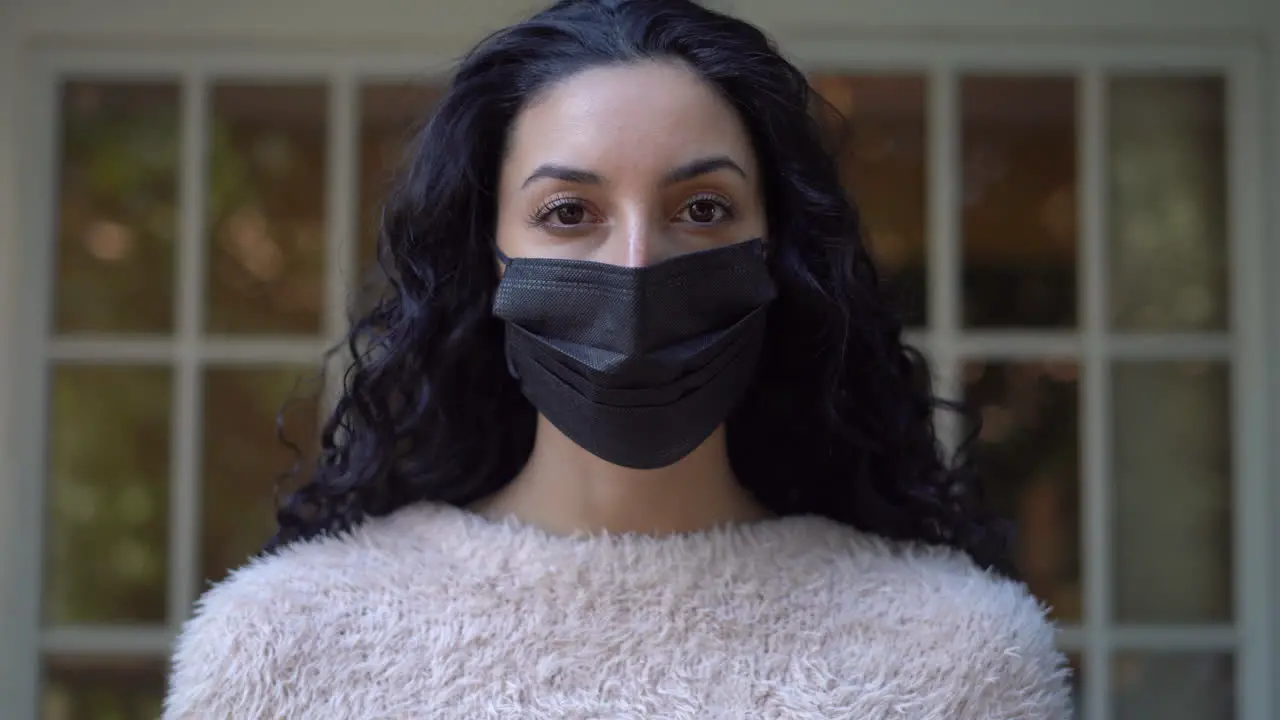 Young attractive Latina woman makes sure her face mask fits properly then removes it while looking at the camera