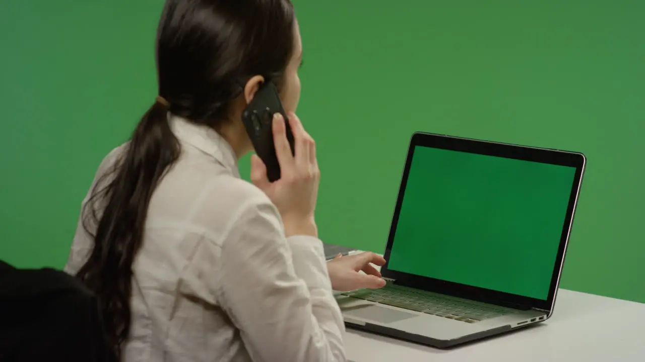 Businesswoman working on laptop answers phone on green screen