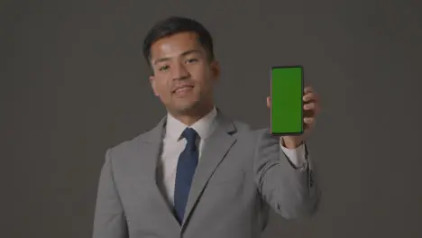 Studio Shot Of Smiling Businessman In Suit Holding Green Screen Mobile Phone