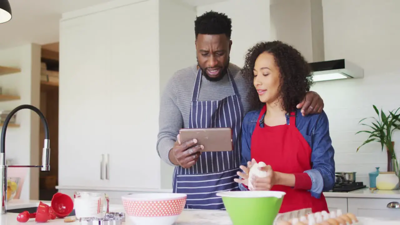 Happy african american couple wearing aprons using tablet and baking together