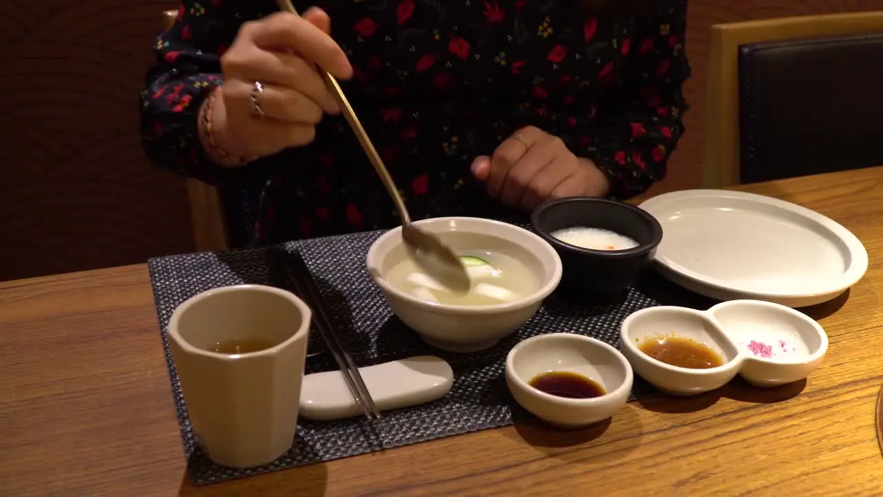 Woman eating Dongchimi Korean radish water kimchi showing on spoon close-up in restaurant