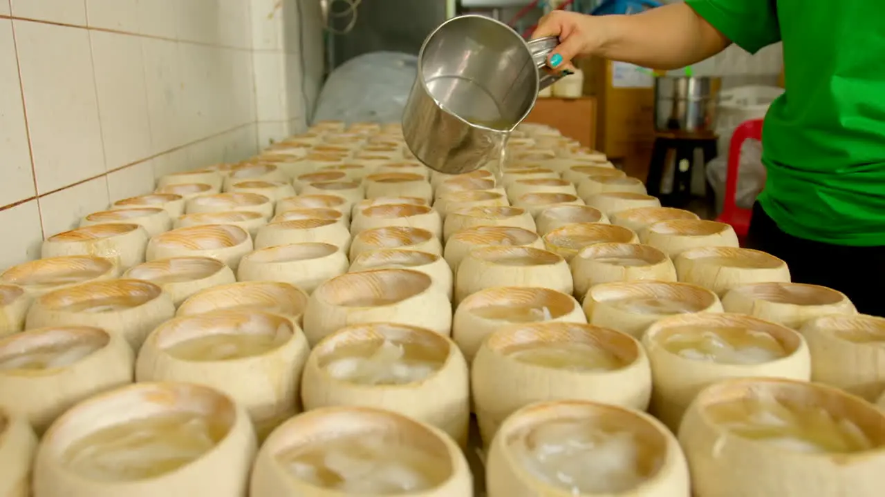 Unidentifiable person pouring hot coconut water jelly into empty shell