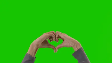 Studio Close Up Shot Of Woman Making Heart Shape Symbol For Love Against Green Screen