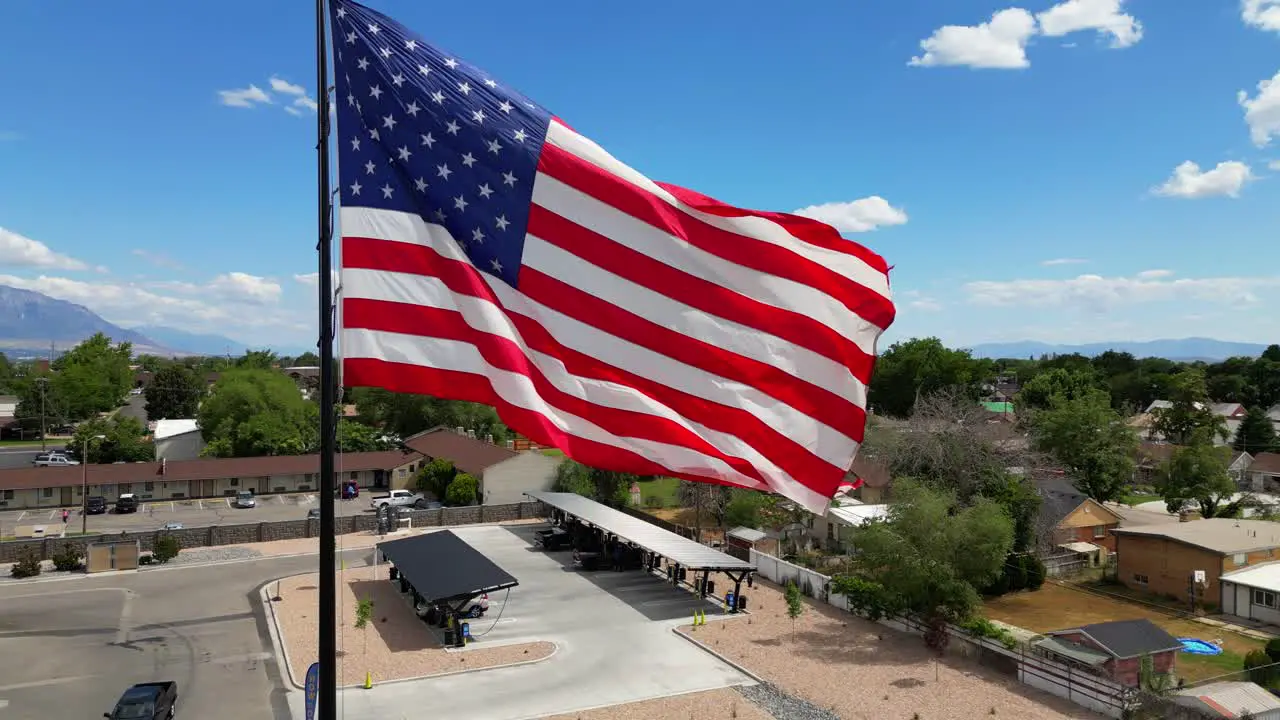 American flag USA blowing waving in the wind on beautiful sunny summer day with clouds and blue skies overlooking mountains drone slowly panning clockwise around flagpole in 4K 60fps