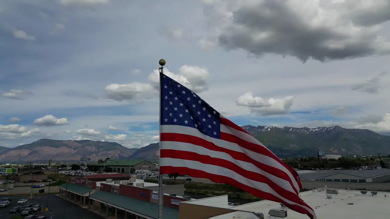 American flag USA blowing waving in the wind on beautiful sunny summer day with clouds and blue skies overlooking mountains and small town as drone quickly pans rotates left in 4K 60fps