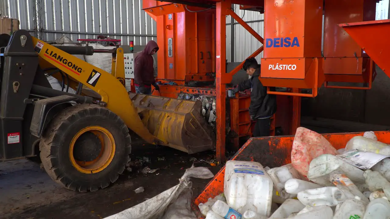 Medium view of workers loading compacted waste onto a bulldozer inside a waste processing plant