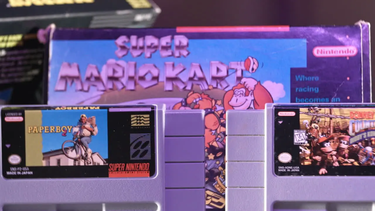 Vintage Super Nintendo Cartridges with Box in Background in Purple Light SLIDE LEFT