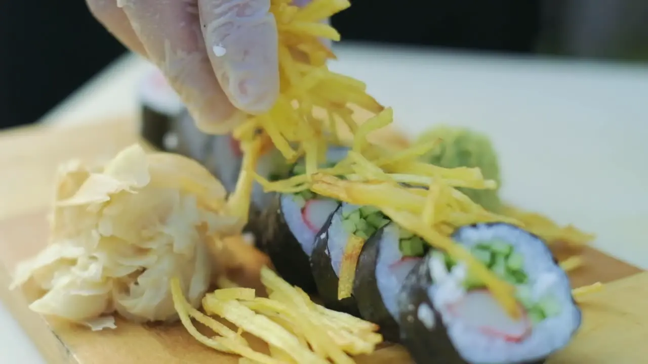 Close-up shot of fresh Japanese sushi on plate with restaurant chef decorating rolls with chips serving preparing