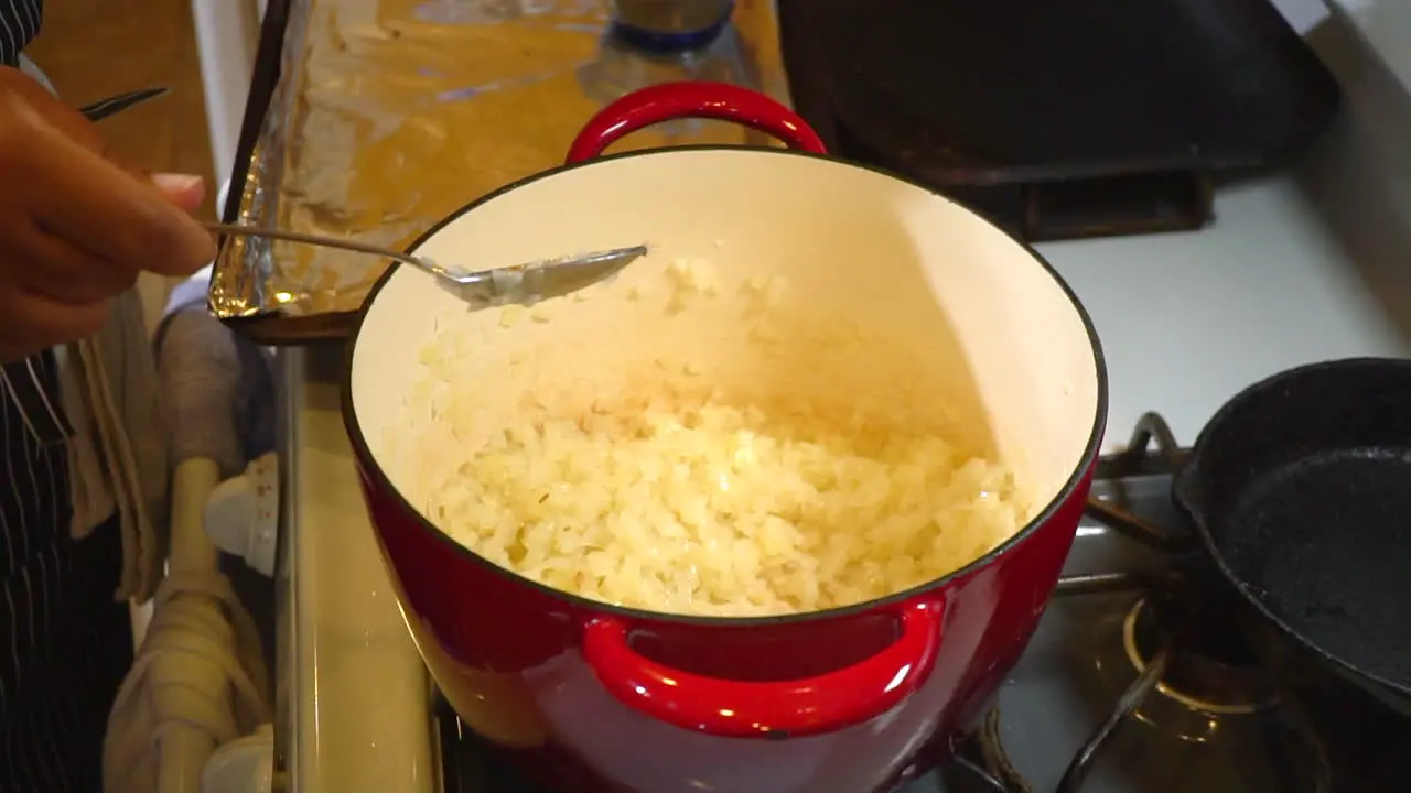 Woman adds ingredients to onions in pot for chili base Slowmo Closeup