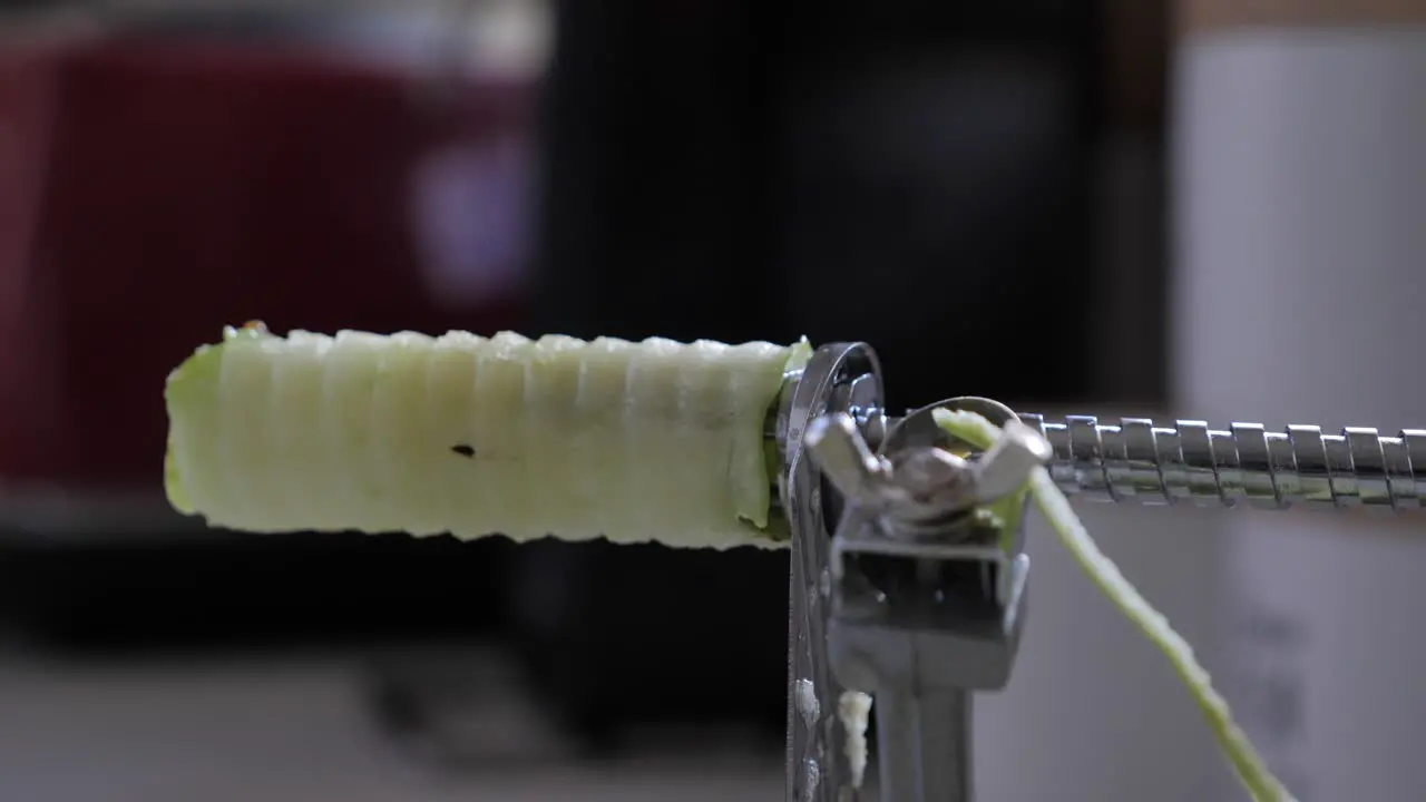 Mans hand grabs at green apple and pulls away from core on silver metallic device on kitchen bench