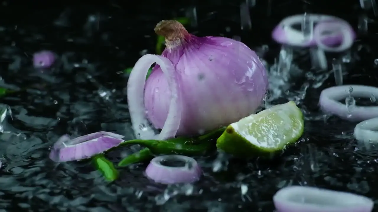 Slow Motion Reversed Shot of Onion Rings and an Onion a Lime Quarter and Green Chilis being Splashed with Rain Water