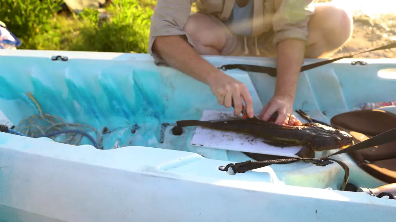 A man cutting into the meat of a flathead fish on his kayak in Australia