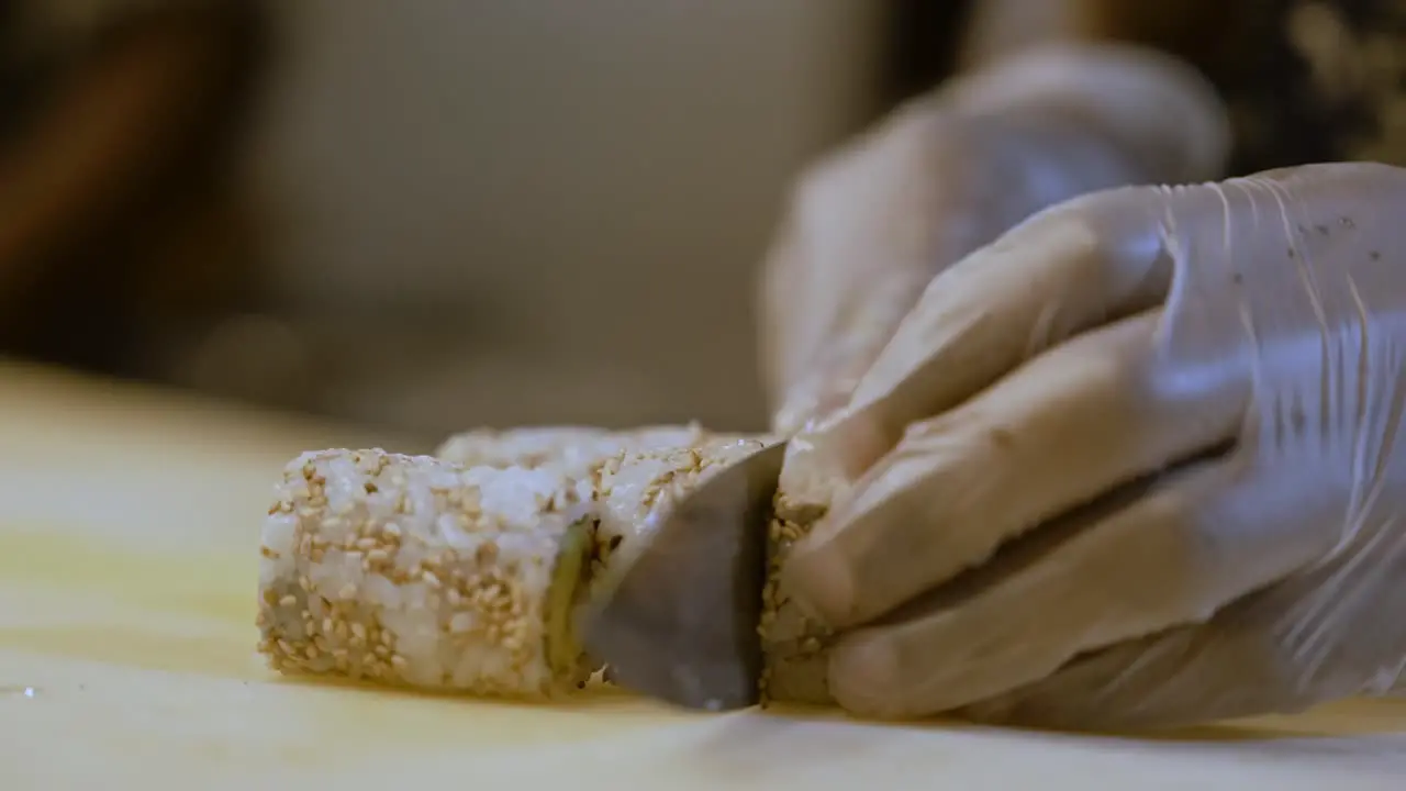 Person Wearing Gloves Cutting Sushi Roll In Slices Homemade Preparation