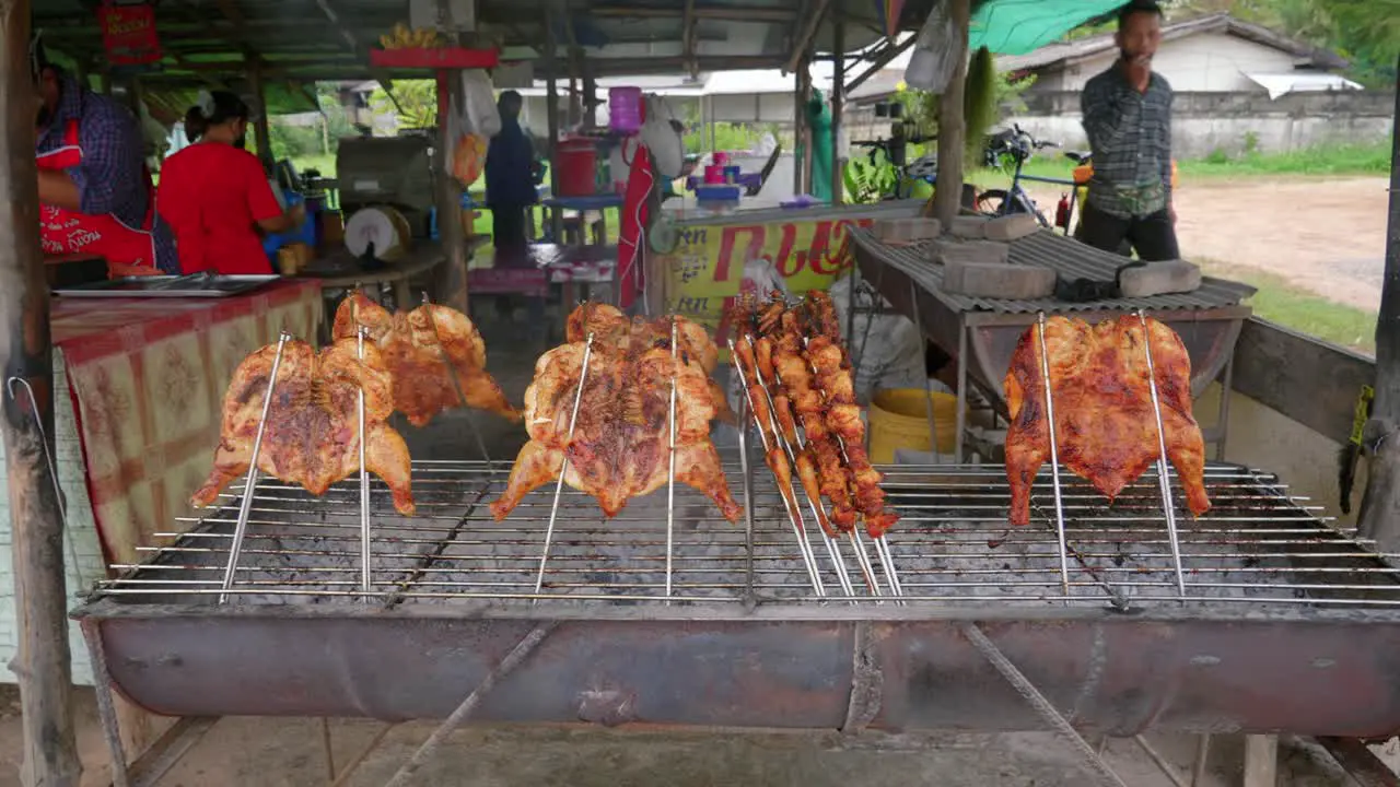 Asian cooks grilling barbecued chicken skewers at an outdoor street market