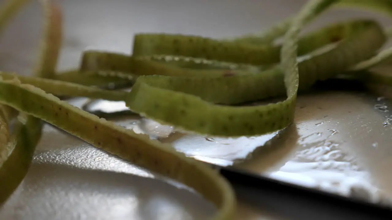 Slow motion pan over metal sharp knife with green apple peel covering it and water droplets