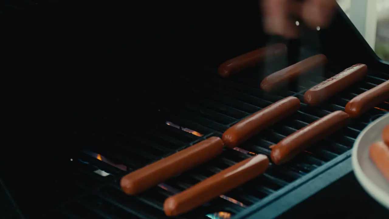 Placing hotdogs on grill with metal tongs