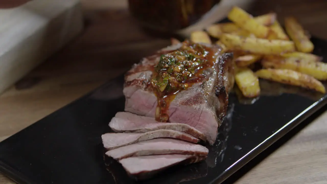 Spooning chimichurri sauce to slices meat with french fries