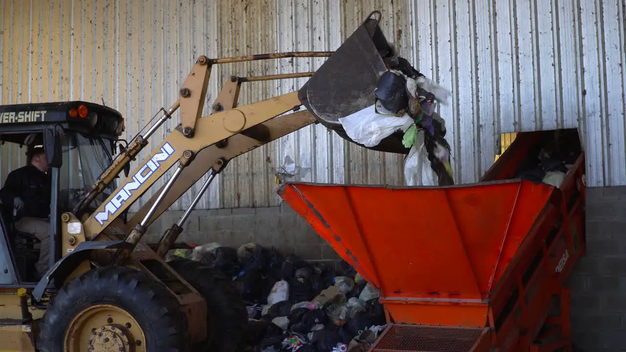 A bulldozer's bucket dumping the waste into a conveyor belt's hopper inside a waste processing plant