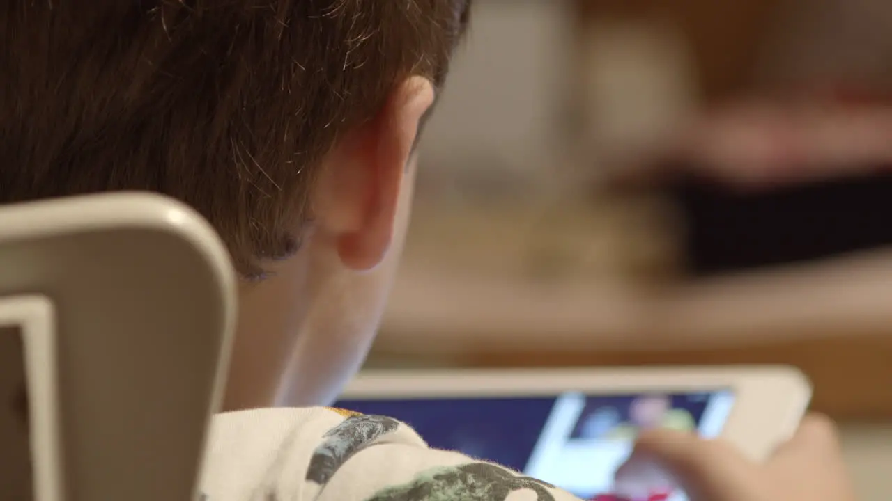 Over the shoulder as young boy watches video on tablet close-up