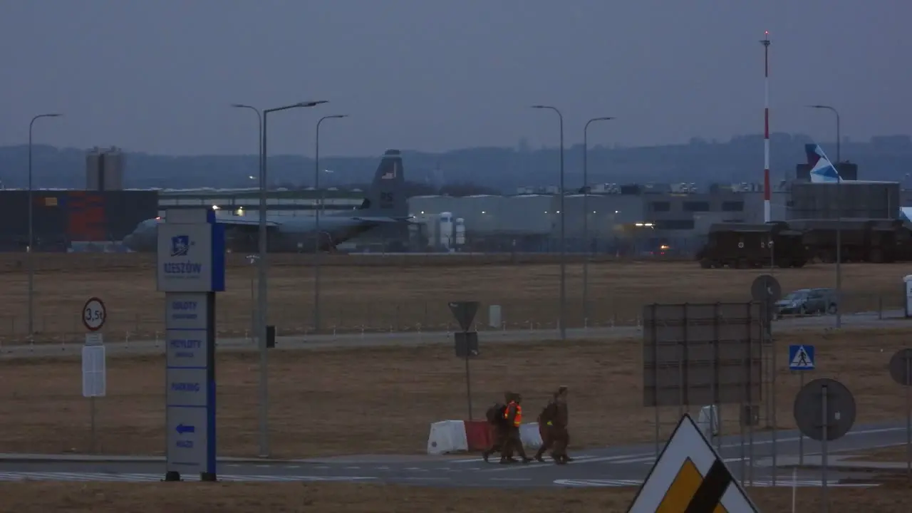 A military cargo plane awaits takeoff in the distance four airport security personnel cross a road