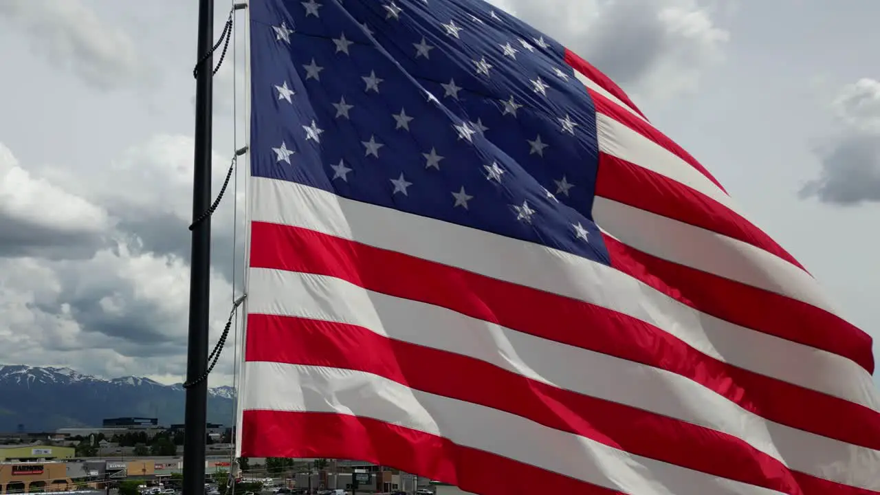 American flag USA blowing waving in the wind on beautiful sunny summer day with lots of puffy white clouds and blue skies overlooking Wasatch Mountains as drone flies around flag pole in 4K 60fps