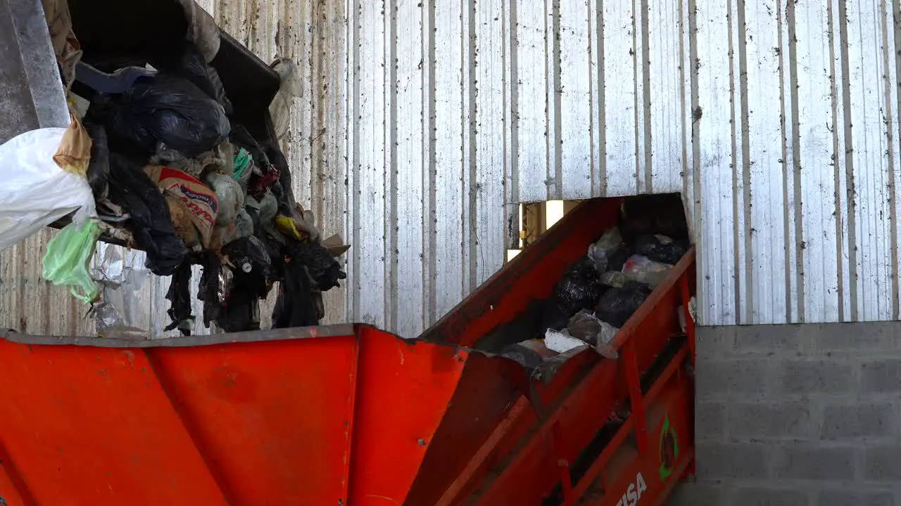 A bulldozer's bucket dumps the waste into a conveyor belt's hopper inside a waste processing plant