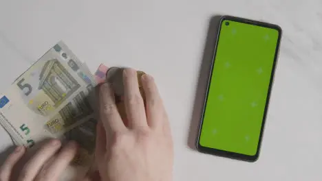 Overhead Currency Shot Person Counting Euro Notes And Coins Next To Green Screen Mobile Phone