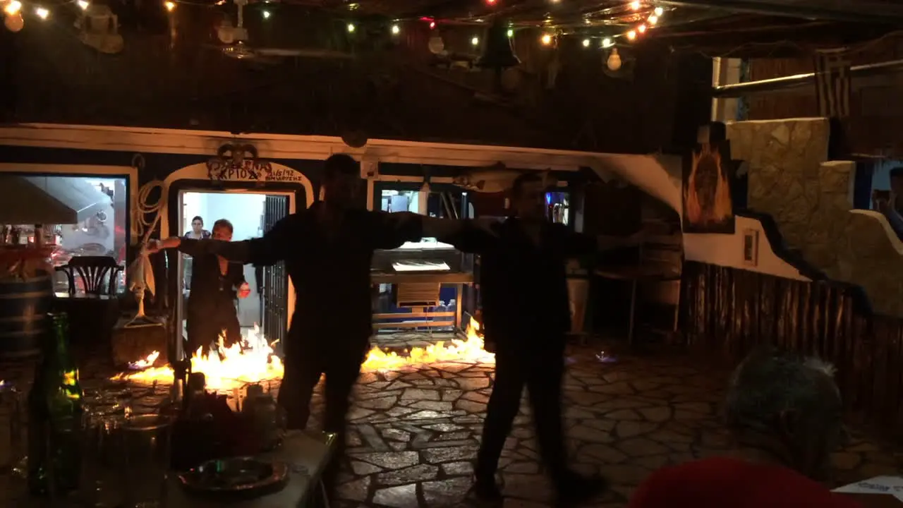 Two waiters dancing traditional greek dance in front of fire in local greek pub