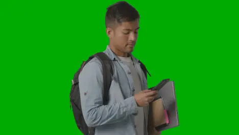 Portrait Of Smiling Male University Or College Student Looking At Mobile Phone Against Green Screen 1