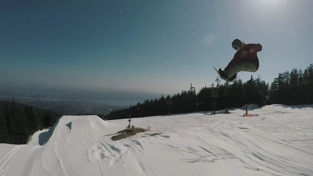 Follow camera shot of Snowboarder jumping and performing a 360 spin at Grouse mountain park in slow motion